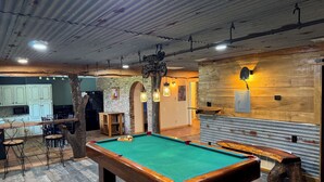 Un tavolo da biliardo in una stanza dal design rustico, con pareti in mattoni a vista e elementi in legno.