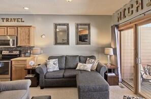 A living room with a grey sectional sofa, two side tables with lamps, a kitchen area with wooden cabinets, and a sliding glass door leading to an outdoor patio. - Skiing , golf or nearby lakes. Schuss has it all! (Bellaire)