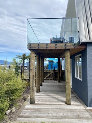 Une maison moderne dotée d’une terrasse en bois, d’un balcon en verre et offrant une vue sur l’océan.
