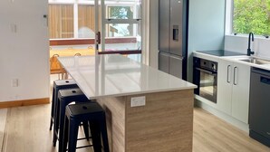 A modern kitchen with a central island, wooden flooring, and a view to the outdoors. - Totara Bach - just a few meters away from the beach (Tata Beach, Golden Bay) (Tata Beach)