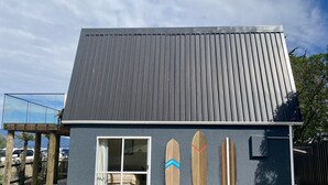 A modern house with a sloped roof, a large window, and a wooden deck. - Totara Bach - just a few meters away from the beach (Tata Beach, Golden Bay) (Tata Beach)