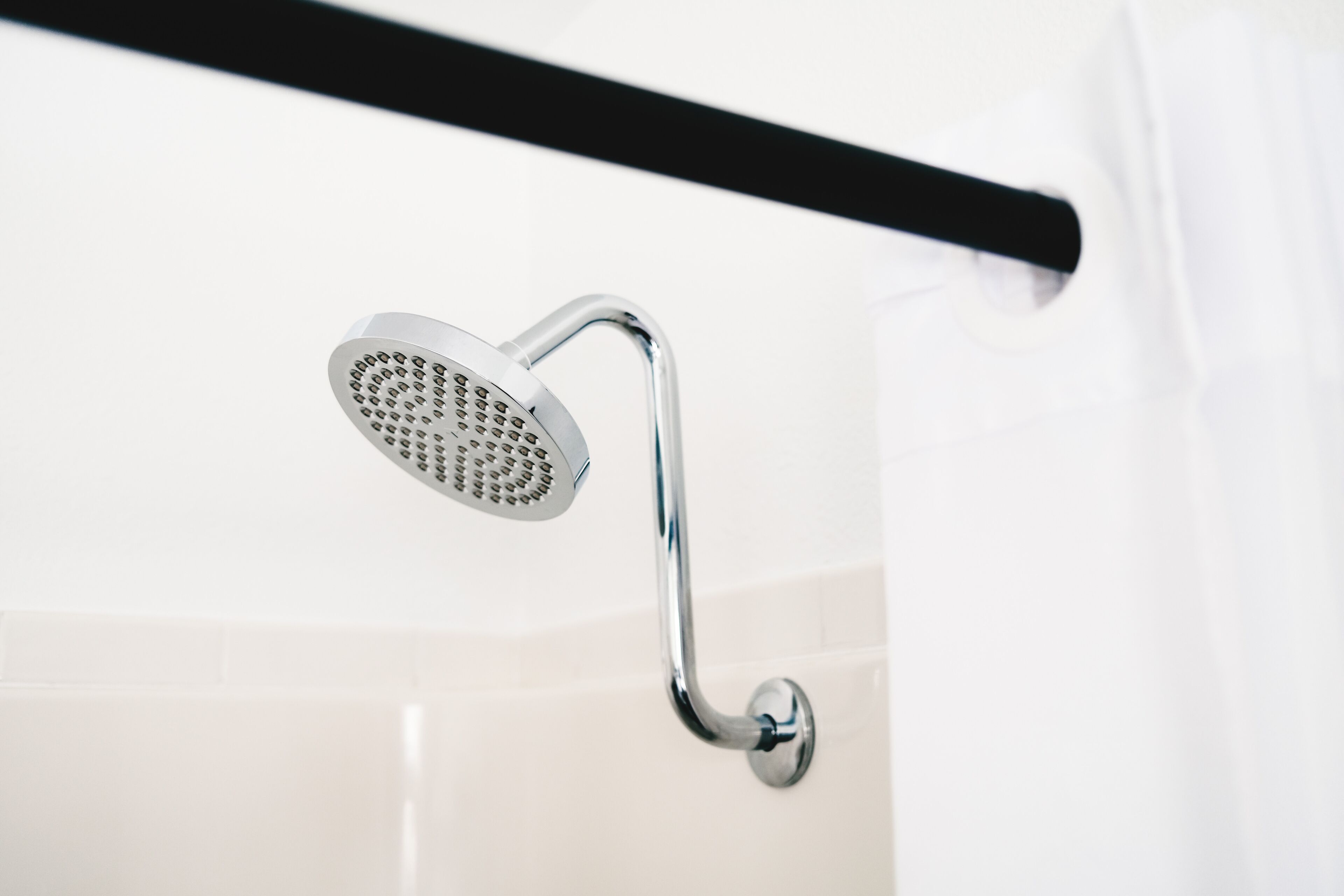A chrome showerhead mounted on a wall with a black towel bar above it.