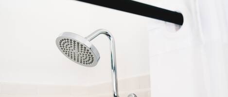 A chrome showerhead mounted on a wall with a black towel bar above it.
