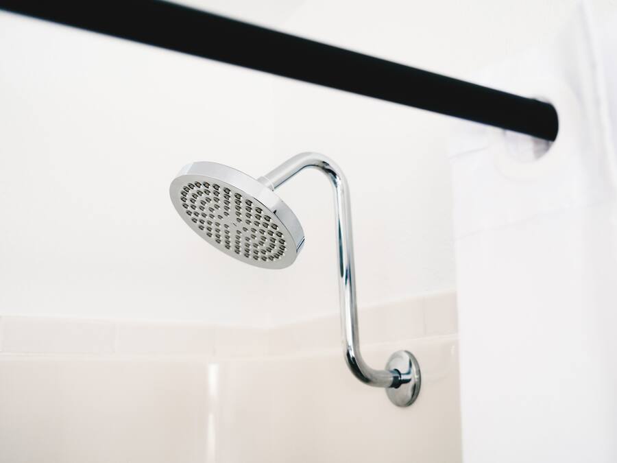 A chrome showerhead mounted on a wall with a black towel bar above it.