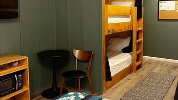 A room with a bunk bed labeled 'Warren' and 'Helen', a small table, a microwave, a chair, and a patterned rug.