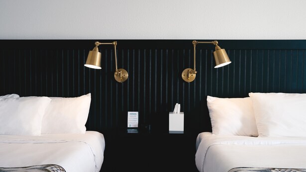 A hotel room with two beds, a dark wall with vertical lines, and two gold lamps. - Jackalope Motor Lodge (Pinedale)