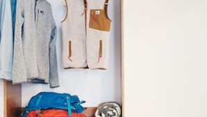 A closet with hanging clothes, a folded jacket, and a blue backpack. - Jackalope Motor Lodge (Pinedale)