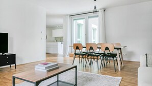 Ein modernes Wohnzimmer mit Couchtisch aus Holz, Fernseher und Essbereich mit Stühlen und Tisch.
