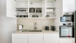 Eine moderne Küche mit weißen Schränken, einer Granit Arbeitsplatte, einer Edelstahlspüle und eingebauten Geräten, darunter eine Kaffeemaschine, ein Toaster und ein Backofen.