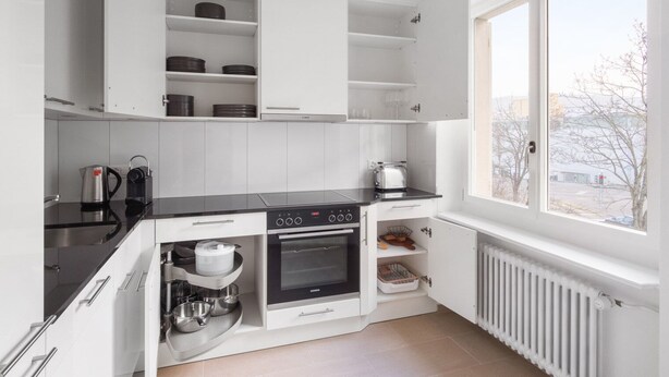 A modern kitchen with white cabinets, a black countertop, a built-in oven, and a window with a view of the outside. - Luxe Oerlikon 3.5 Room w/ Balcony, 1min to Train Station, by Blueground (Zurich)