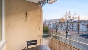 A balcony with a wooden bench, a view of a street with cars and buildings, and a clear sky. - Luxe Oerlikon 3.5 Room w/ Balcony, 1min to Train Station, by Blueground (Zurich)