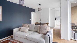 A modern living room with a grey sofa, two pendant lights, and a view into a dining area. - Luxe Oerlikon 3.5 Room w/ Balcony, 1min to Train Station, by Blueground (Zurich)