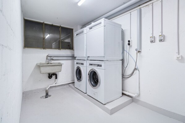 A laundry room with two stacked washing machines, a sink, and a window.