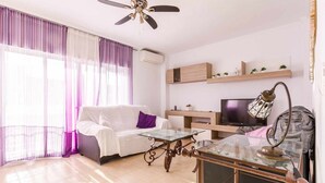 Una sala de estar moderna con un sofá blanco, una mesa de centro de vidrio y un televisor sobre un mueble de madera.