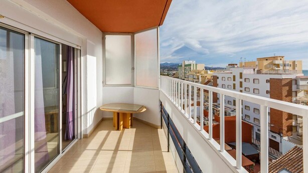 Un balcón con mesa y sillas, ventanas amplias y vistas de edificios aledaños.