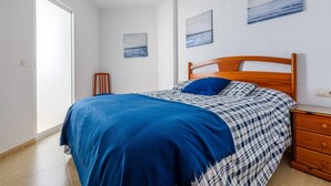 Un dormitorio con cama, mesita de noche, cabecera de madera y dos cuadros colgados en la pared.