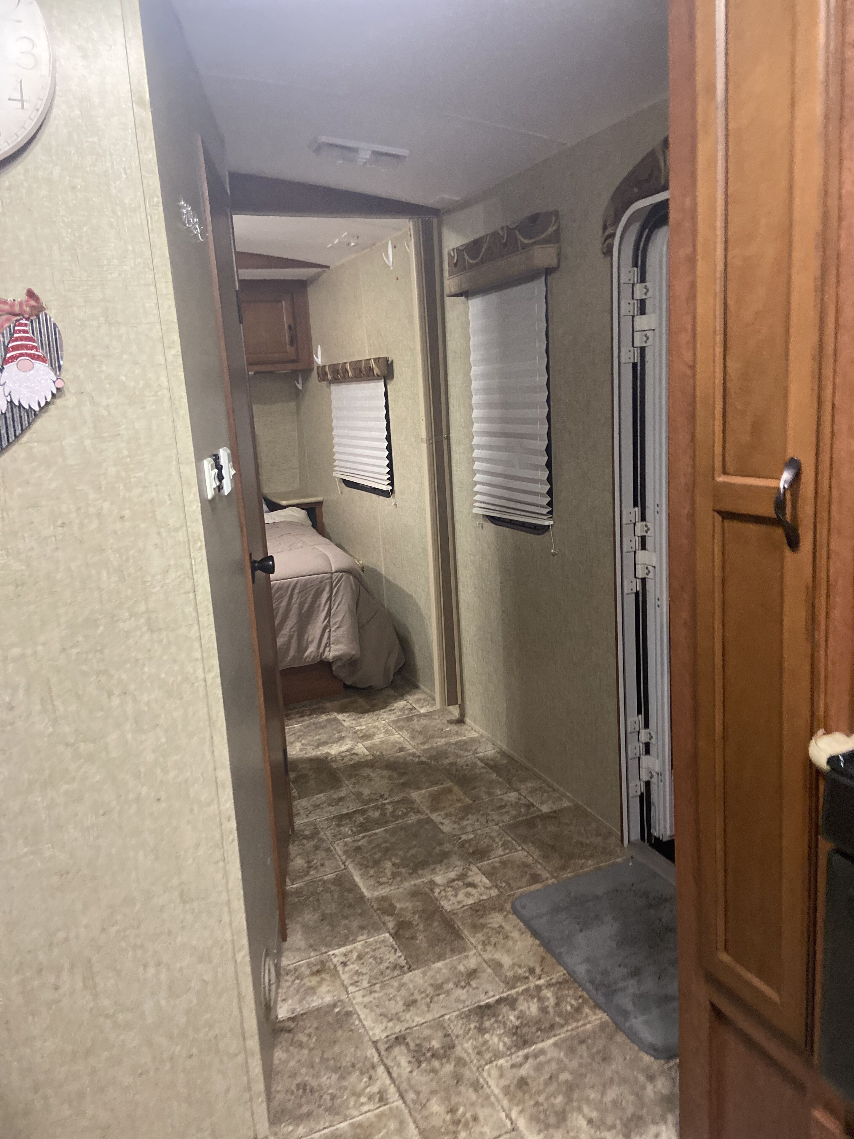 A narrow hallway with a bed, a door, and a window with blinds.