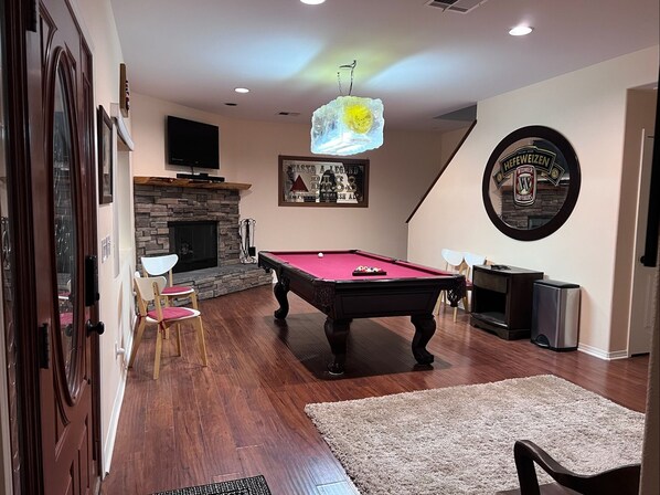 A cozy living room with a pool table, a fireplace, and a mounted television.
