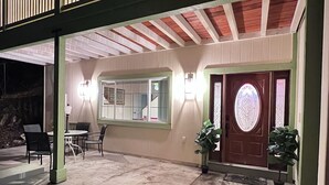 A covered patio area with a table and chairs, a door with a stained glass window, and a potted plant. - Mountain Escape: Sleeps Multiple Families with Pool Table & Game Room (Running Springs)