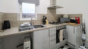 Een moderne keuken met raam, spoelbak, fornuis, magnetron en waterkoker.