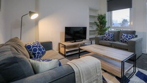 Een moderne woonkamer met een bank, salontafel, televisie en een plant.