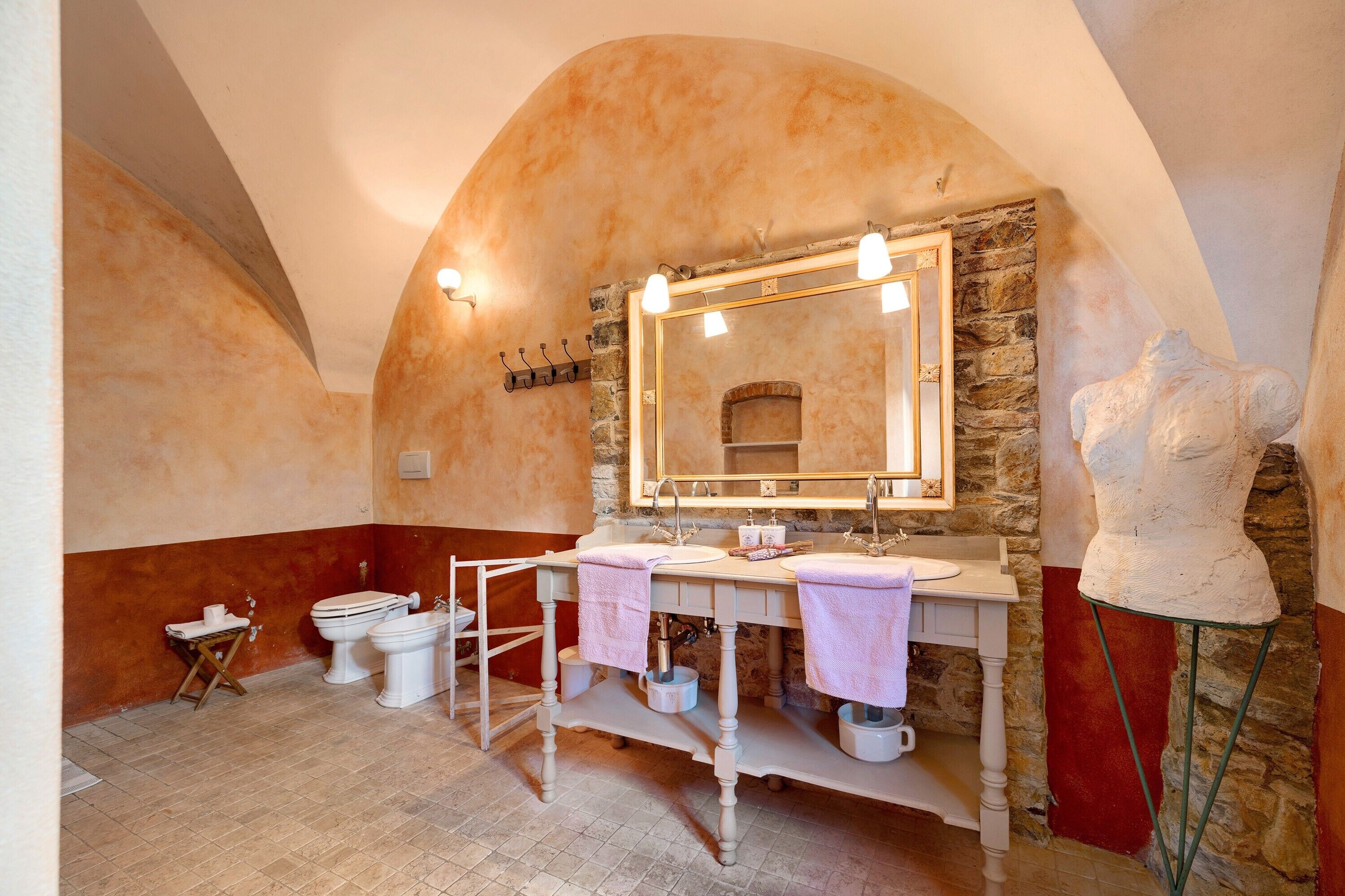 Un bagno con parete in pietra, uno specchio grande, due lavandini, un bidet e una scultura.