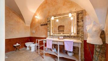 Un bagno con parete in pietra, uno specchio grande, due lavandini, un bidet e una scultura.