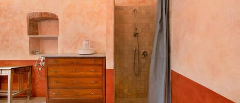 A bathroom with a wooden vanity, a shower with a tiled wall, and a small shelf with toiletries.