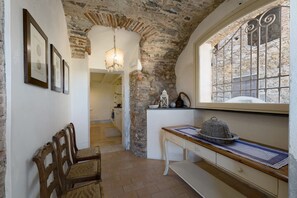 Una habitación con pared de piedra, muebles de madera, un escritorio con un sombrero y una ventana con vistas.