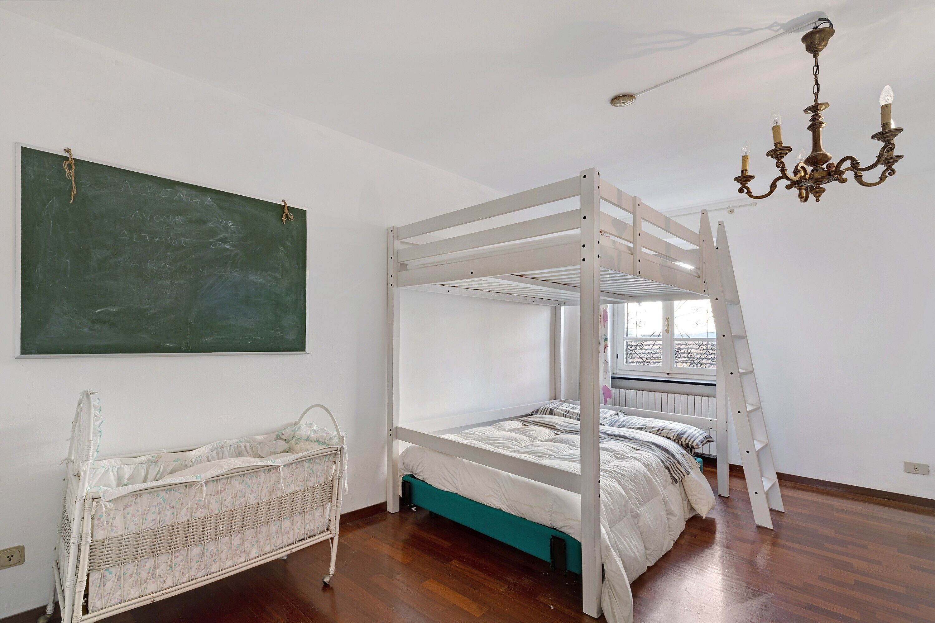Une chambre avec un lit superposé, un tableau noir, un berceau et une échelle.