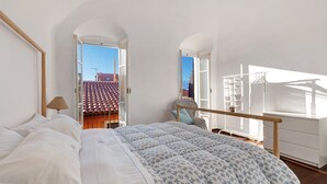 Ein Schlafzimmer mit Bett, Fenster und Blick auf ein rotes Ziegeldach.