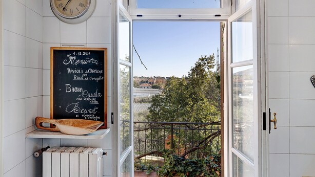 Eine Küche mit einer Kreidetafel-Speisekarte, einer Holzschüssel und Blick auf einen Balkon mit Grünpflanzen.