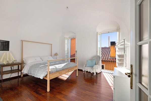 Une chambre à coucher avec un lit en bois, une chaise, un bureau et une vue sur un balcon.