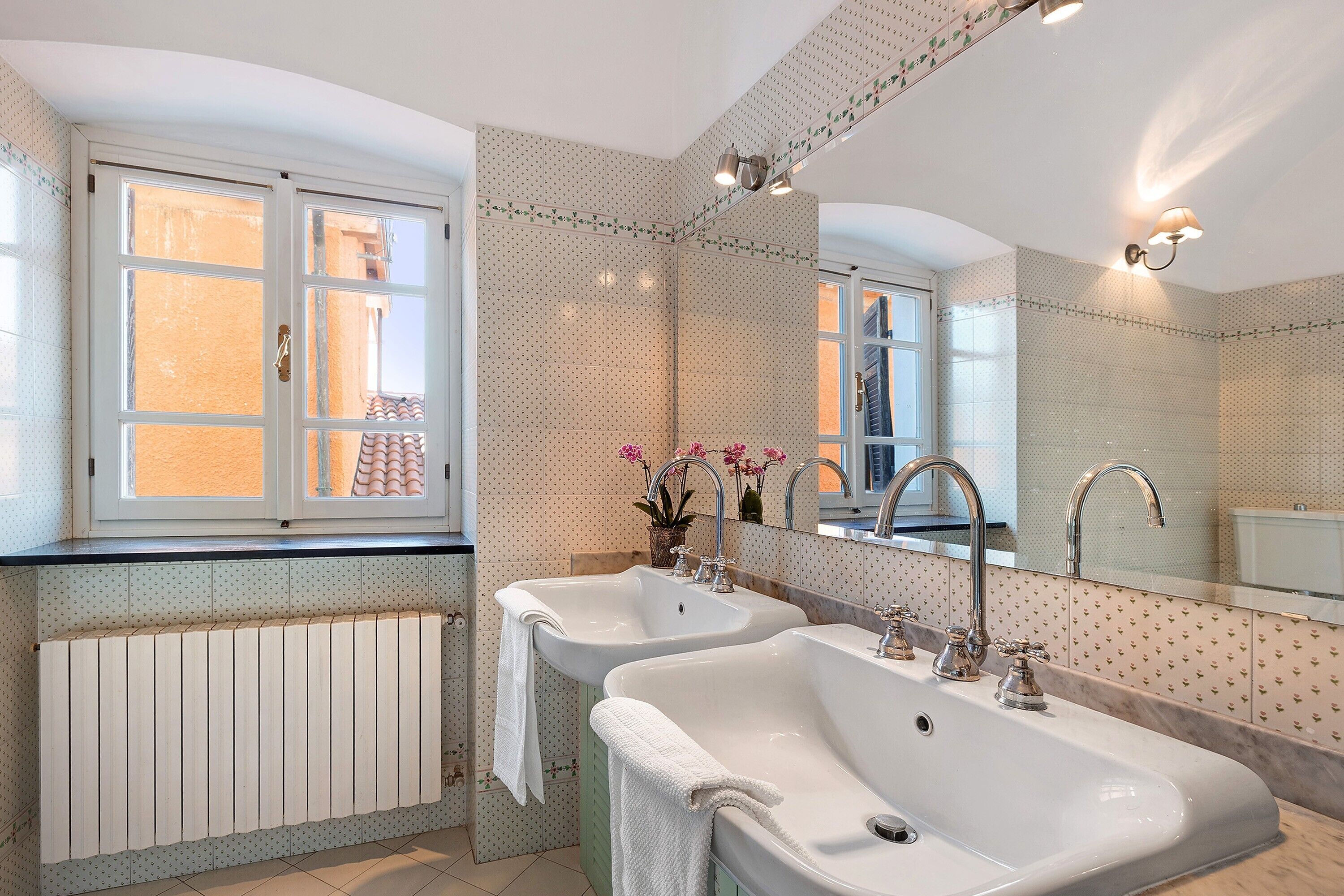 A bathroom with two sinks, a window, a radiator, and a mirror.