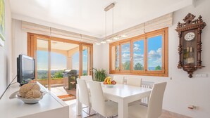 Un espace repas avec une table blanche, des chaises, une horloge et une vue dégagée grâce à de grandes fenêtres.