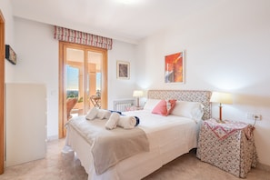 Un dormitorio con cama, mesitas de noche, un radiador, una puerta que da a un espacio exterior y una ventana con vistas.