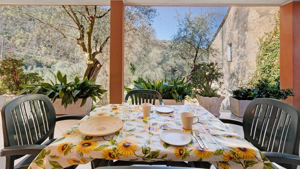 A table set outdoors with a sunflower tablecloth, surrounded by chairs, and potted plants. - Apartment 'Succu La Taggiasca' with Mountain View & Terrace (Stellanello)