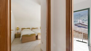A bedroom with two beds, a bedside table with a lamp, and a view of a balcony with a railing. - Apartment 'Pana La Taggiasca' with Mountain View (Stellanello)