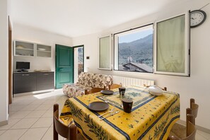 A dining area with a table set for two, a sofa, a television, and a view of the outdoors.
