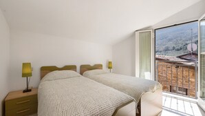 A bedroom with a bed, nightstand, lamp, and a balcony with a view. - Apartment 'Pana La Taggiasca' with Mountain View (Stellanello)