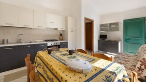 A compact kitchen with a dining area, a small TV, and a green door. - Apartment 'Pana La Taggiasca' with Mountain View (Stellanello)