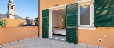 A building with a balcony, a bed, and a window with shutters.
