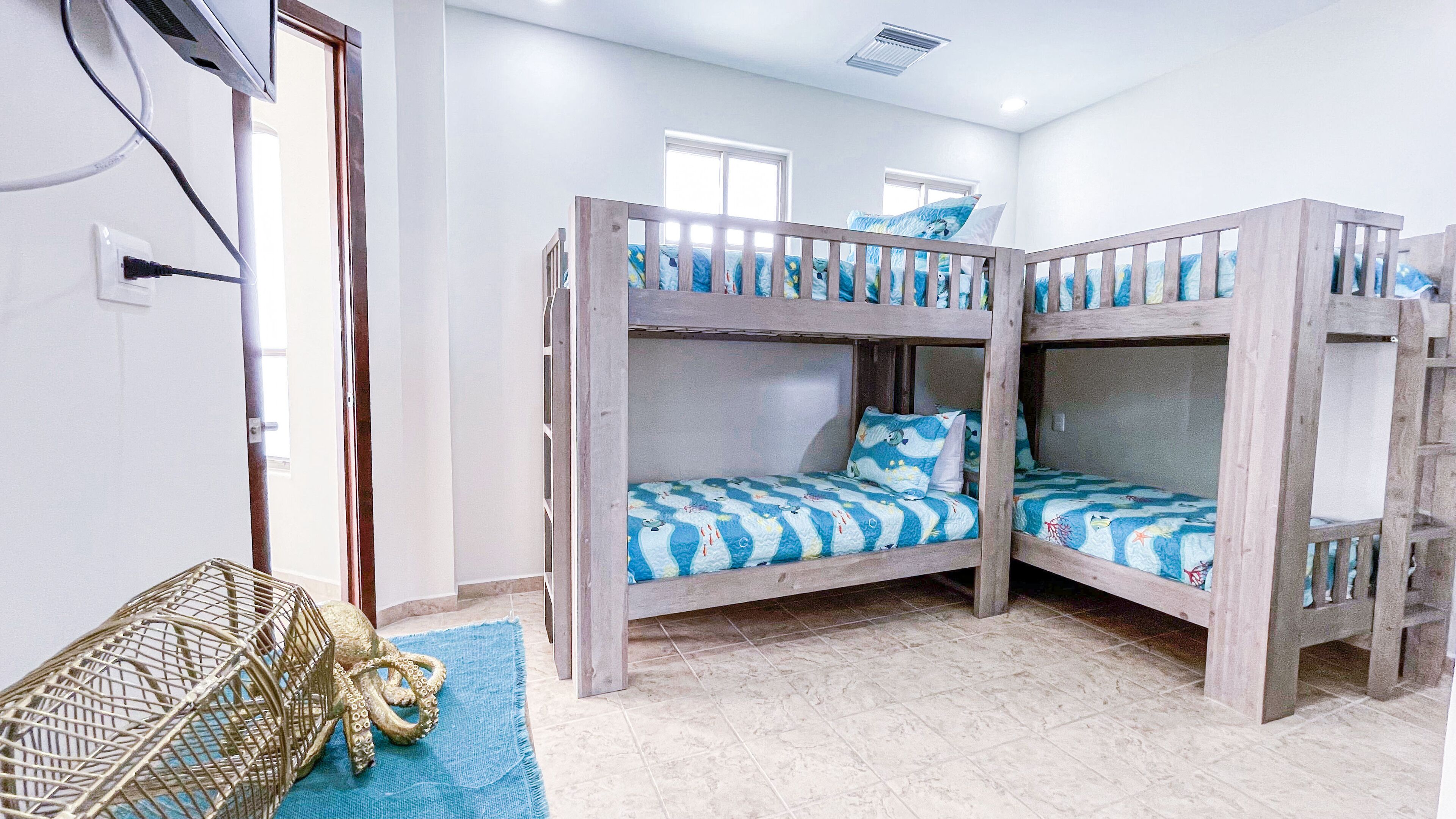 Una habitación con literas, una ventana pequeña y una escultura decorativa de pulpo sobre una alfombra azul.