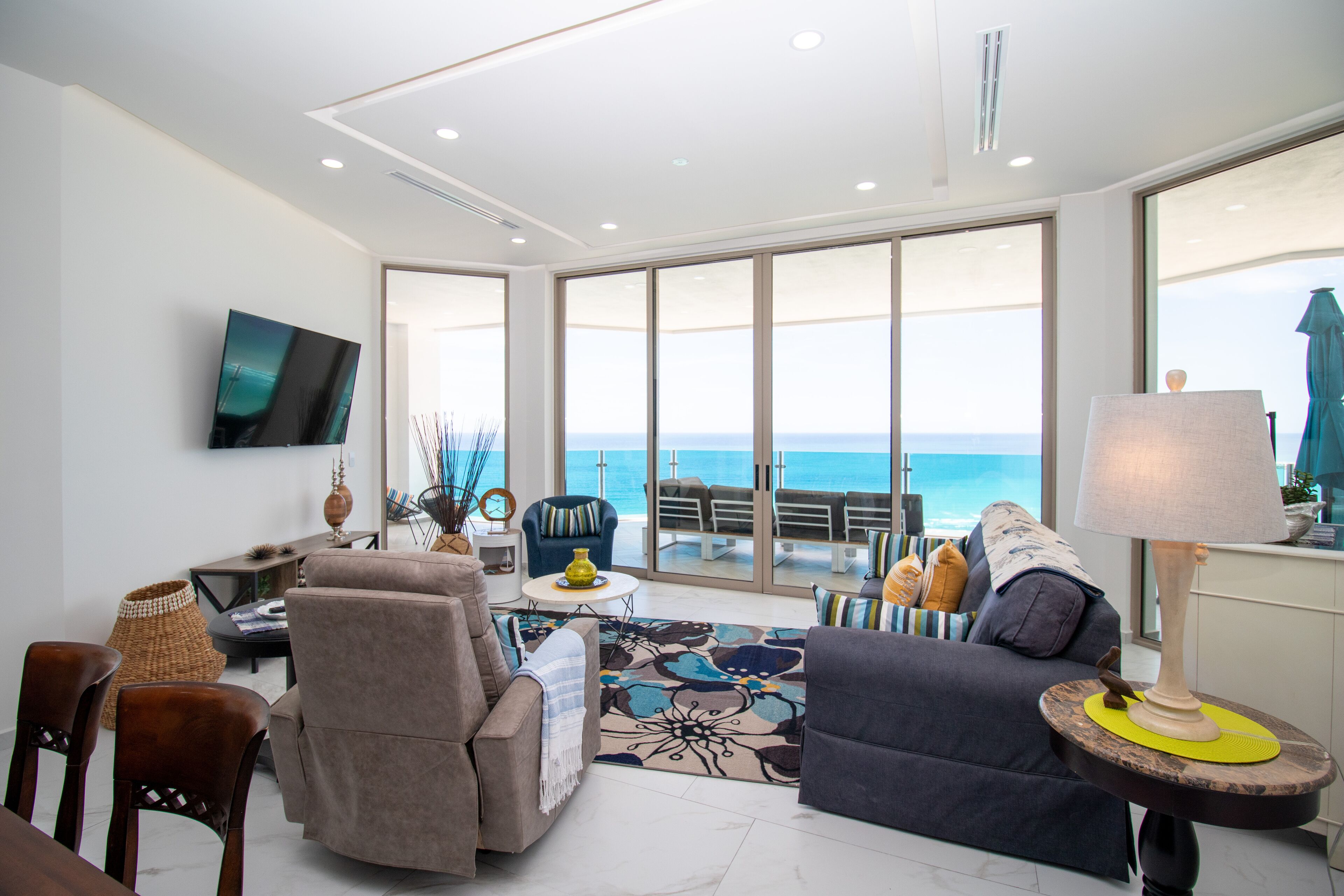 A spacious living area with a large window overlooking the sea, furnished with a sofa, armchairs, and a coffee table.