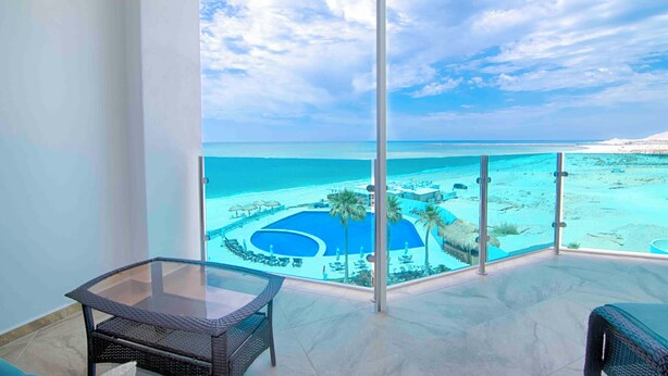 A balcony with a glass table and chairs, overlooking a pool area and beach. - Hotel Esmeralda Beach Resort (Puerto Peñasco)