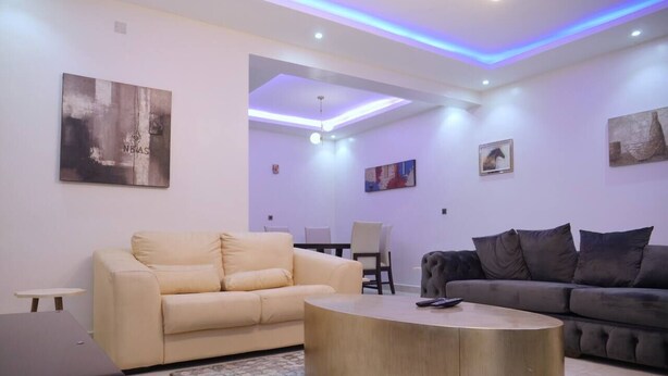 A modern living room with a beige sofa, a dark coffee table, and a grey sofa. There are paintings on the walls and a ceiling light fixture.