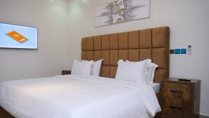 A bedroom with a large bed, a wooden nightstand, and a wall-mounted control panel.