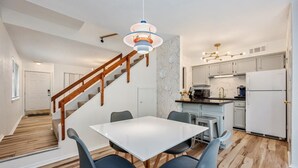 Uma cozinha moderna com armários brancos, uma ilha central e uma área de jantar com mesa branca e cadeiras azuis.