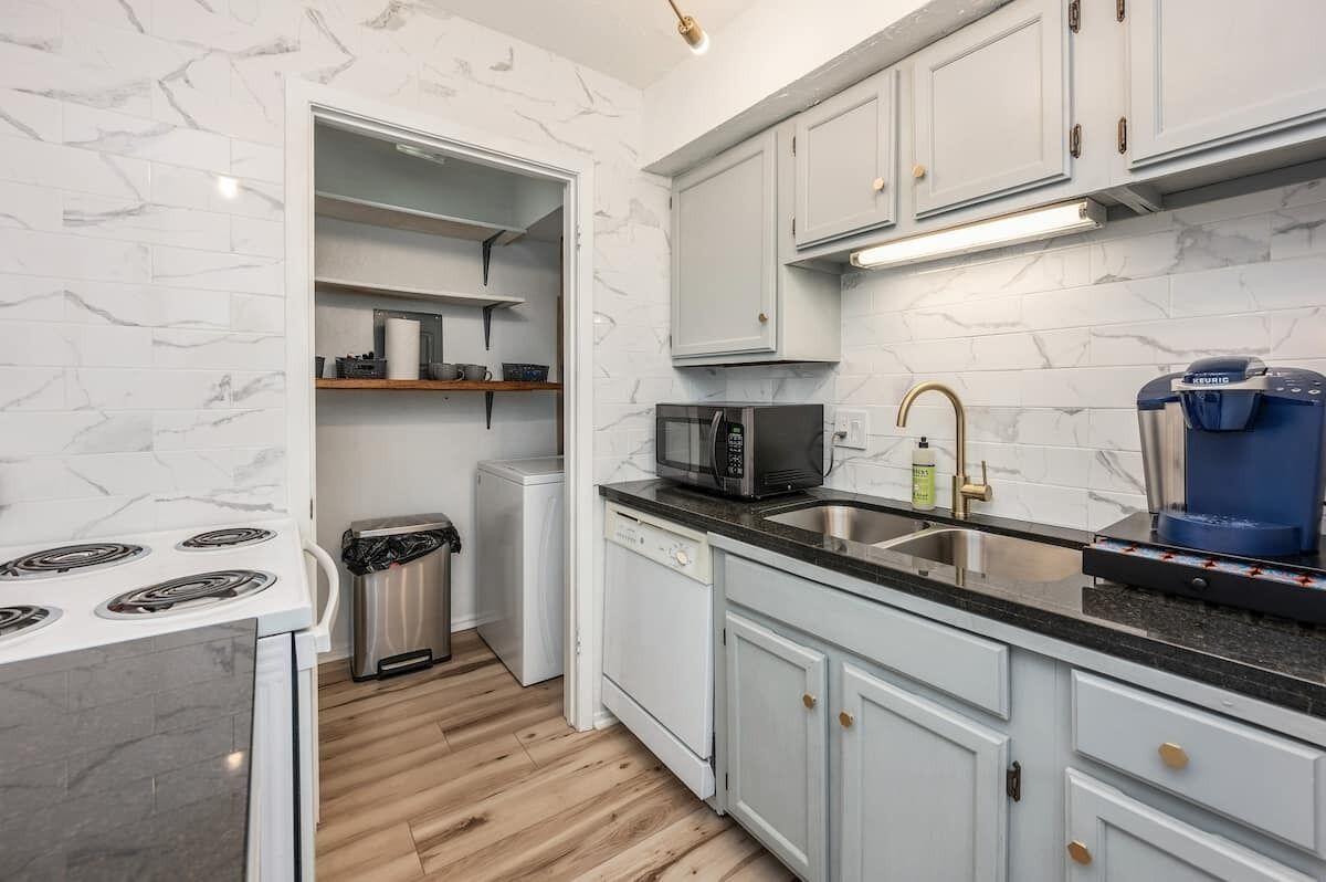 A modern kitchen with white cabinets, a built-in microwave, a coffee maker, and a dishwasher.