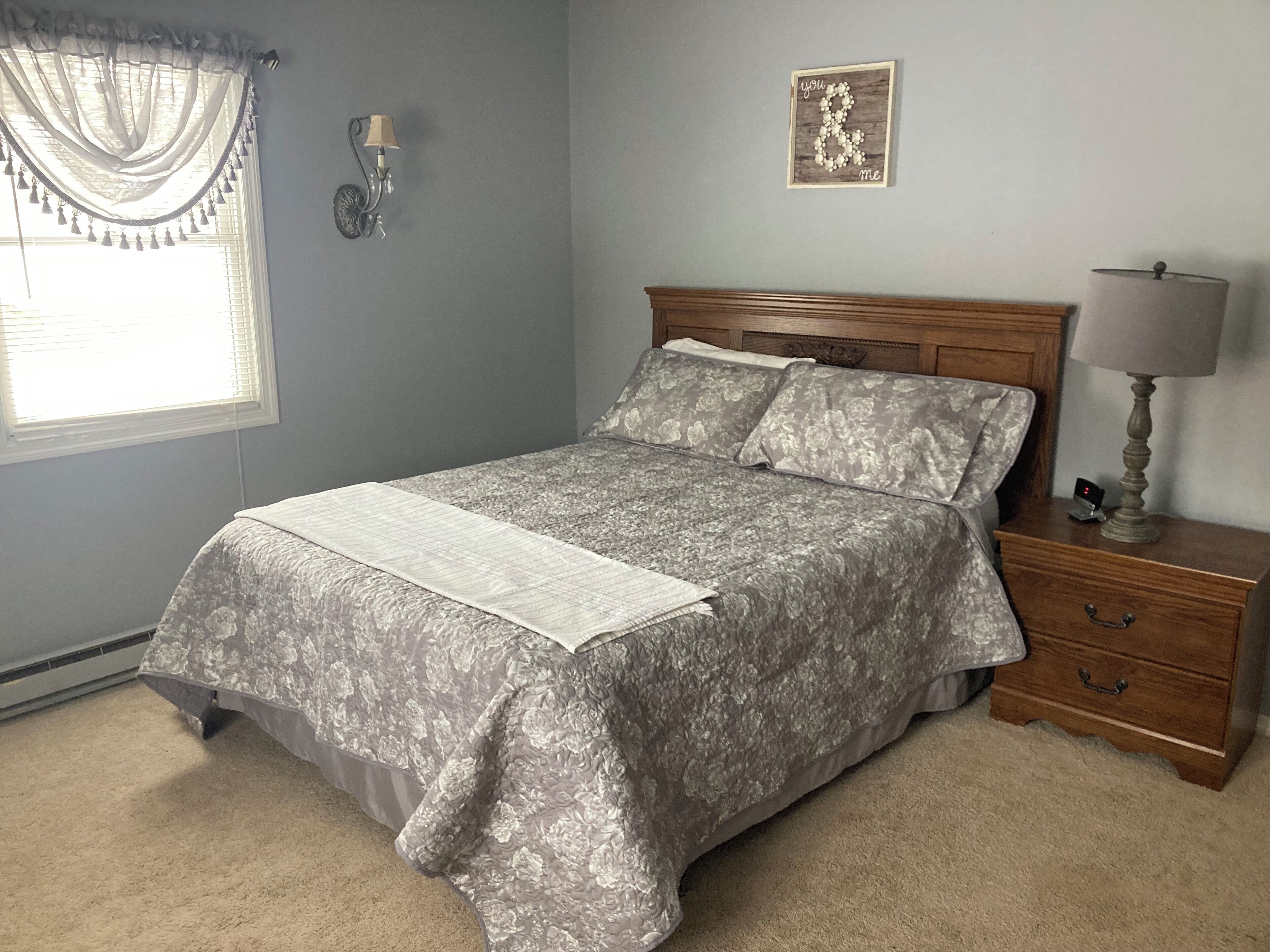 A bedroom with a bed, a nightstand, a lamp, a wall clock, and a decorative wall piece.